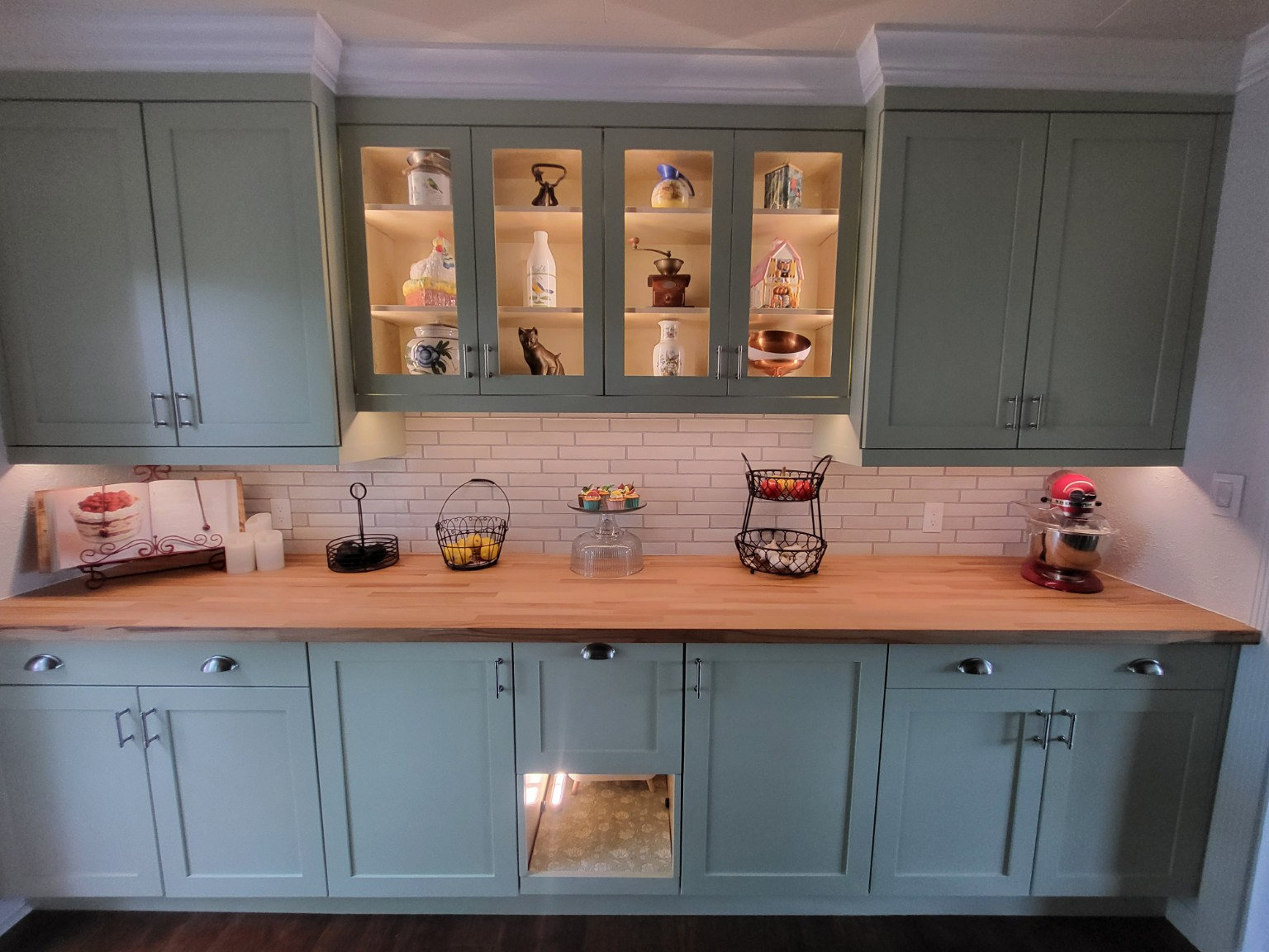 Custom sage green kitchen cabinetry and illuminated glass cabinets